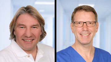 Zwei Männer, einer mit blonden Haaren in einem weißen Hemd, der andere mit Brille in blauer Arbeitskleidung, stehen nebeneinander.