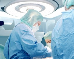 Chirurgisches Team in Schutzkleidung führt einen Eingriff in einem Operationssaal durch, umgeben von medizinischen Geräten und Beleuchtung.