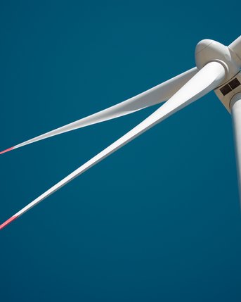 Windkraftanlage mit langen, weißen Rotorblättern vor klarem, blauem Himmel.