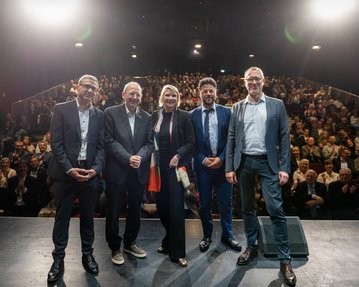 Foto: SRH-Vorstand Patrick Mombaur, Mannheims Oberbürgermeister Christian Specht, Cathryn Clüver Ashbrook, Moderator Nabil Atassi und NTM-Intendant Christian Holtzhauer lächeln in die Kamera, hinter ihnen das Publikum der Mannheimer Reden