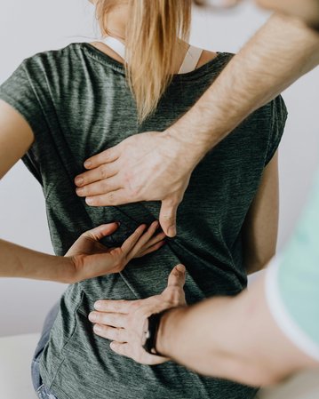 Eine Person erhält eine Rückenmassage von einem Therapeuten, der beide Hände auf den unteren Rücken der Person platziert hat.